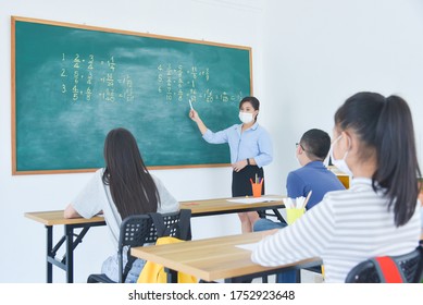 Asian Teacher Wearing Facial Mask While Teaching Students At School,all Of Student Wearing Facial Mask And Sitting Far Away From Each Other.