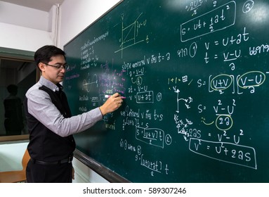 Asian Teacher Writing The Physics Formula In Thai Language On Black Board In School Classroom, School Education Concept