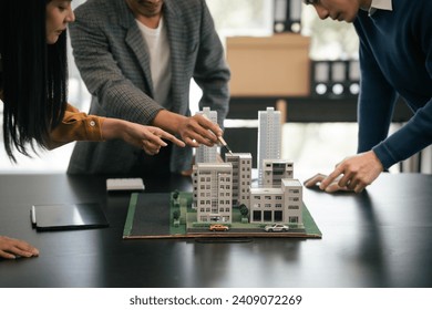 Asian team is engaged in a lively discussion over a scale model of a cityscape, likely representing a real estate or architectural project. - Powered by Shutterstock