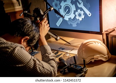Asian technical engineer feeling stressed while repairing drone with computer and other tools on desk. Male technician fixing or maintenance drone. Unmanned aerial vehicle (UAV) photography concept