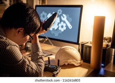 Asian technical engineer feeling stressed while repairing drone with computer and other tools on desk. Male technician fixing or maintenance drone. Unmanned aerial vehicle (UAV) photography concept