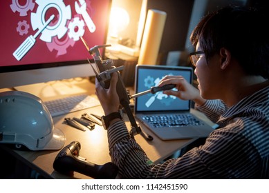 Asian technical engineer using screwdriver for repairing drone with computer and other tools on desk. Male technician fixing or maintenance drone. Unmanned aerial vehicle (UAV) photography concept