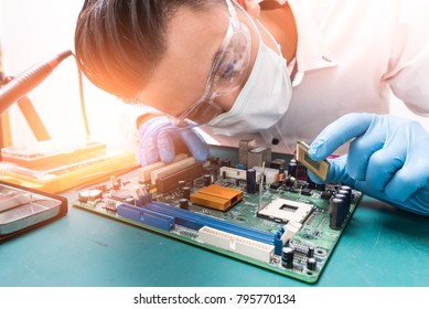 The Asian Technician Is Putting The CPU On The Socket Of The Computer Motherboard. The Concept Of Computer Hardware, Repairing, Upgrade And Technology.