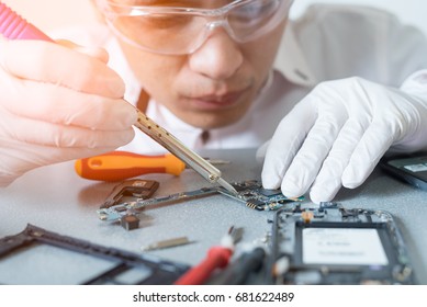 The Asian Technician Repairing The Smartphone's Motherboard By Soldering In The Lab. The Concept Of Computer Hardware, Mobile Phone, Electronic, Repairing, Upgrade And Technology.