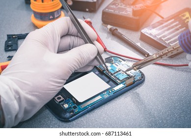 The asian technician repairing the smartphone's motherboard by soldering in the lab. the concept of computer hardware, mobile phone, electronic, repairing, upgrade and technology.