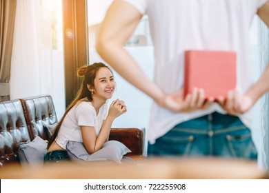 Asian Teen Couple Watching TV. Man Hiding Gift Behind His Back To Bring It Give To A Women.