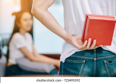 Asian Teen Couple Watching TV. Man Hiding Gift Behind His Back To Bring It Give To A Women.