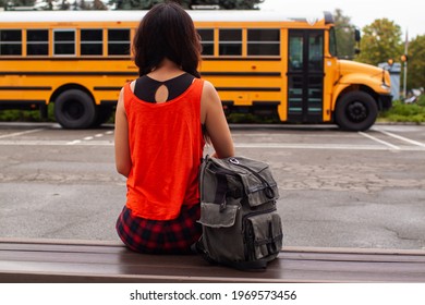 Asian Teen Girl Standing By A Big Yellow School Bus Door With Her Backpack.