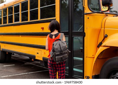 Asian Teen Girl Standing By A Big Yellow School Bus Door With Her Backpack.