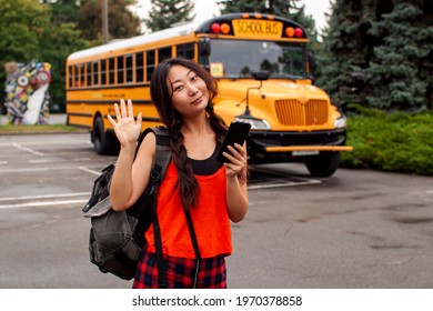 Asian Teen Girl Standing By A Big Yellow School Bus Door With Her Backpack.