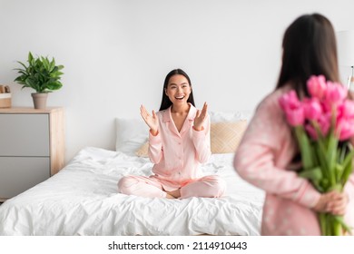 Asian Teen Girl With Tulips Bouquet, Back And Happy Young Female Sitting On Bed In Bedroom Interior. Daughter Congratulates Mom At Birthday, At Home, Surprise For Holiday And Facial Expression, Indoor