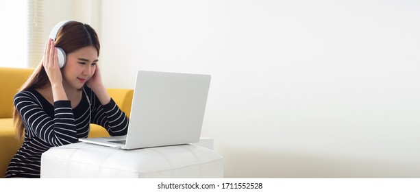 Asian Teen Girl Wearing Headphones Learning Language Online Looking At Screen Laptop Computer During School Closures And The Need For Social Distancing. Homeschooling And Learning While At Home