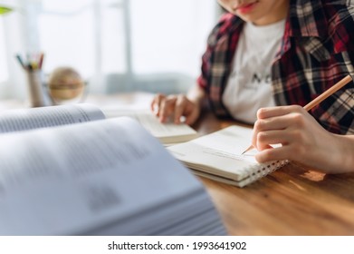 Asian Teen Girl Wearing Headphones Learning Language Online, Using Laptop, Looking At Screen, Doing School Tasks At Home, Writing Notes, Listening To Lecture Or Music, Distance Education