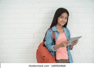 asian teen holding tablet and stand against the brick wall - Powered by Shutterstock