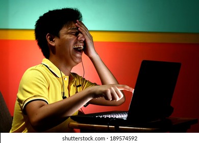 Asian Teen Playing or Working on a Laptop Computer and Laughing. Photo of an asian teen playing or working on a laptop computer and laughing.