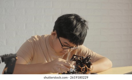 Asian teenage boy connecting wires to circuit board of robotic car with robotic arm at home, STEM education, robotics, and coding for young engineers.