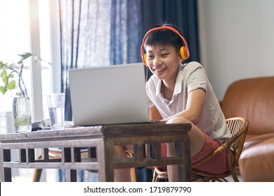 Asian teenage boy taking online lessons at home wearing headset smiling
