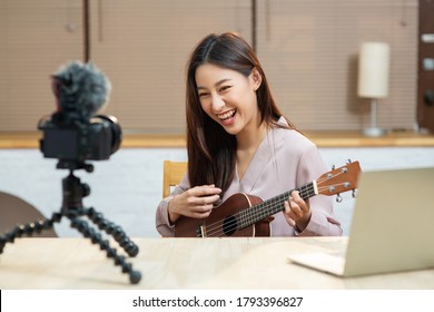 Asian teenage girl look at camera filming her self and playing ukulele guitar