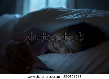 Asian teenage girls lie smart phone on line in the night on the bed at home