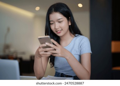 Asian teenage student woman using smartphone to chatting with friends and surfing social media after watching lecture video online lesson on laptop and studying about education knowledge in cafe. - Powered by Shutterstock