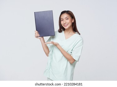 Asian Teenage Woman Wearing A Patient Gown Holding A Policy Book For Assurance In Life With A Smiling Face, Insurance Concept.