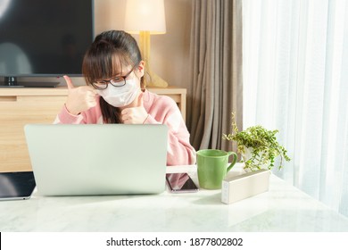 An Asian Teenager Girl With Face Mask Using Laptop Computer In The Living Room To Video Call With Friends Or Family While Quarantine During Covid 19 Pandemic. Lock Down, Physical Distancing, Isolation