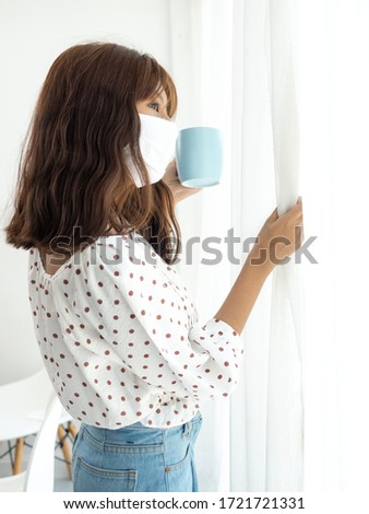 Asian teenager girl wearing mask holding coffee mug and looking out window, corona virus concept.