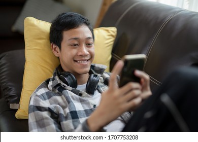 Asian Teenager Smiling And Having Fun While Using Mobile Phone To Talk And Chat With His Tutor At Home. Online Class And Education Or E-learning Concept.