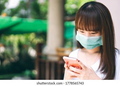 Asian Teenager Student College Wear Mask For Protect Corona Virus. Using Smart Phone For Social Media Online At Outdoor. People Social Distance And New Normal Concept.