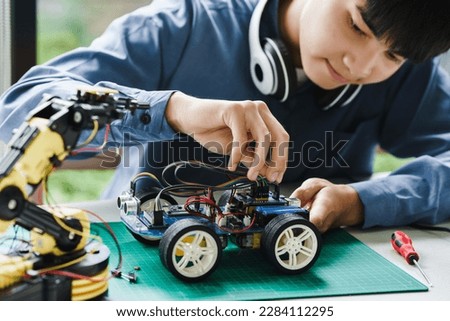 Asian teenager students doing robot arm and robotic cars homework project in house disassemble the circuit and coding. technology of robotics programing and STEM education concept.