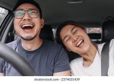 Asian Thai couple smiling, laughing open mouth, happy time while driving a car on road, enjoy vacation holiday, front view. - Powered by Shutterstock