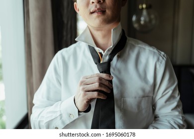 Asian Thai Man On White Shirt Dressing Up And Adjusting Tie On Neck At Home. Neck Tie Dress Up Procedure.