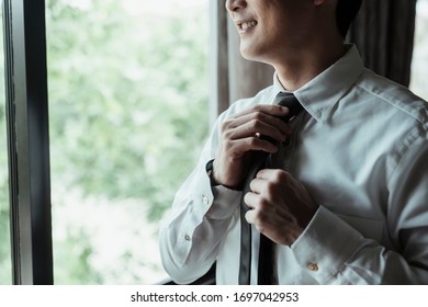 Asian Thai Man On White Shirt Dressing Up And Adjusting Tie On Neck At Home. Neck Tie Dress Up Procedure.