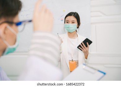 Asian Thai Nurse Giving Presentation To Doctor Inside Hospital Meeting Room. Reading Script On Smartphone Using Internet.