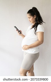 Asian Thai Pregnant Mother Use A  Telephone For Online Shopping  Baby Clothes First Born. Concept Of Buying Baby Supplies.
