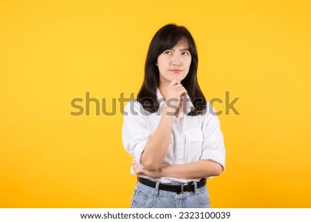 Asian thoughtful woman keeps hand on chin looks pensively above wearing white shirt and jean plants poses against yellow background blank copy space for your advertising content thinks about future.