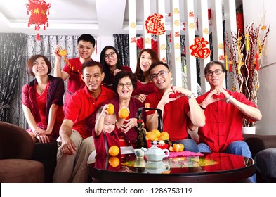Asian Three Generations Family Celebrating Chinese New Year. Some Of The Family Members Making Love Shape With Hands. Chinese Characters In The Photo Means 