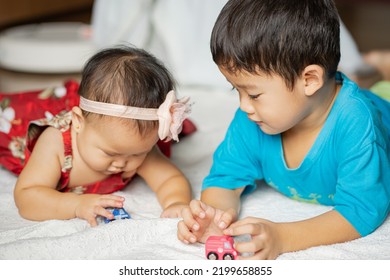 An Asian Toddler And Baby Expresses Their Sibling Love Thru Sharing Toys