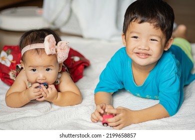 An Asian Toddler And Baby Expresses Their Sibling Love Thru Sharing Toys