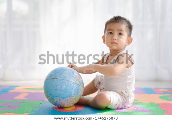 Asian toddler boy is learning through playing\
with the globe model in the house, concept of kid education through\
play and active learning for child development at home, home\
school, home schooling.