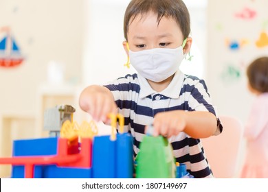 Asian Toddler Boy Playing Toy In Kids Club At Hotel.3.5 Years Old Boy Child Wearing Face Mask In Day Care.Covid-19 Coronavirus.Stay Home.Social Distancing In School.Back To School.New Normal Behavior.