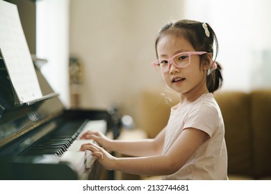 Asian toddler girl look at camera with smiling while playing piano, exploring music instrument, performance, early childhood music education, leisure activity, side view girl kid playing piano. - Powered by Shutterstock