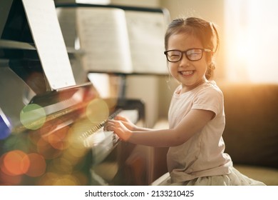 Asian toddler girl look at camera with smiling while playing piano, Happy back to school concept, Early childhood music education, leisure activity, side view girl kid sitting with piano.