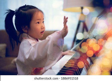 Asian toddler girl look up and learning piano lesson from online class during Covid-19 pandemic lockdown, e-learning, self isolation, new normal lifestyle, music education, early childhood activity