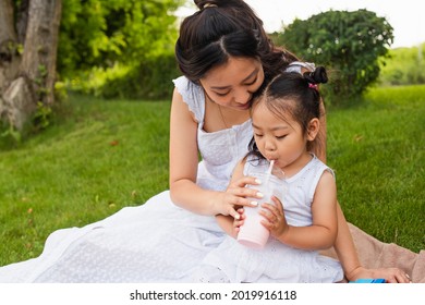 Asian Toddler Kid Drinking Tasty Milkshake Through Straw Near Mother In Park