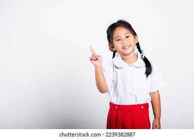 Asian toddler smiling happy wear student thai uniform red skirt keeps pointing finger at copy space in studio shot isolated on white background, Portrait little children girl preschool, Back to school - Powered by Shutterstock