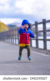 An Asian Toddler In Winter Appearance Winter Jacket Happily Running Hooping Towards Camera At Lake Yamanaka, Japan