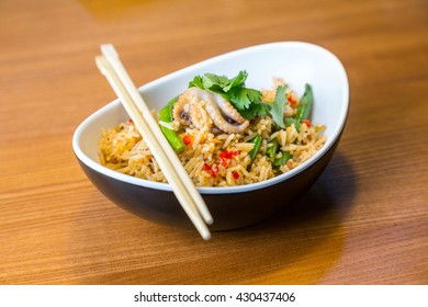 Asian ric�e with tofu and vegetables in oval plate with bamboo sticks on a wooden table in asian restaurant