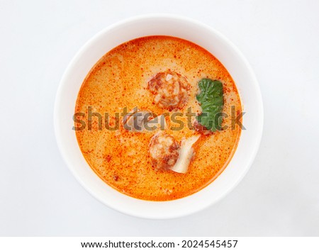 Asian Tom Yam soup with shrimps, coconut milk, tomatoes, lemongrass, mint and cilantro in a white ceramic bowl on a white plate
