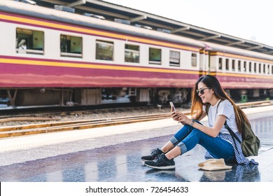 Asian Tourist Teenage Girl At Train Station Using Smartphone Map, Social Media Check-in, Or Buy Ticket Booking. Modern Travel App Technology, Lone Traveler, Summer Vacation Railroad Adventure Concept